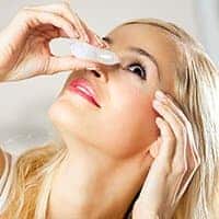 Young woman putting eyedrops in eyes